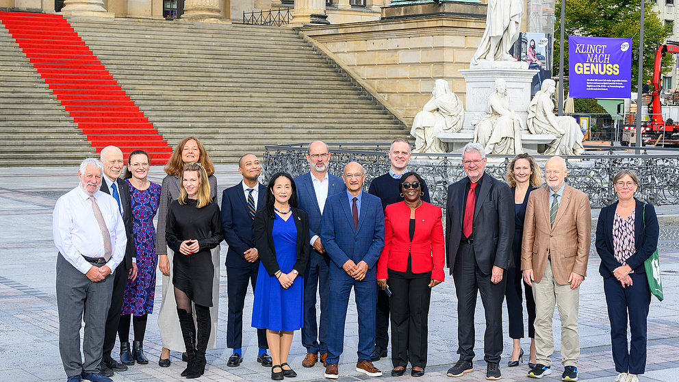 Eine Gruppe von 15 Personen steht vor einer großen Steintreppe mit rotem Teppich und historischen Statuen im Hintergrund.