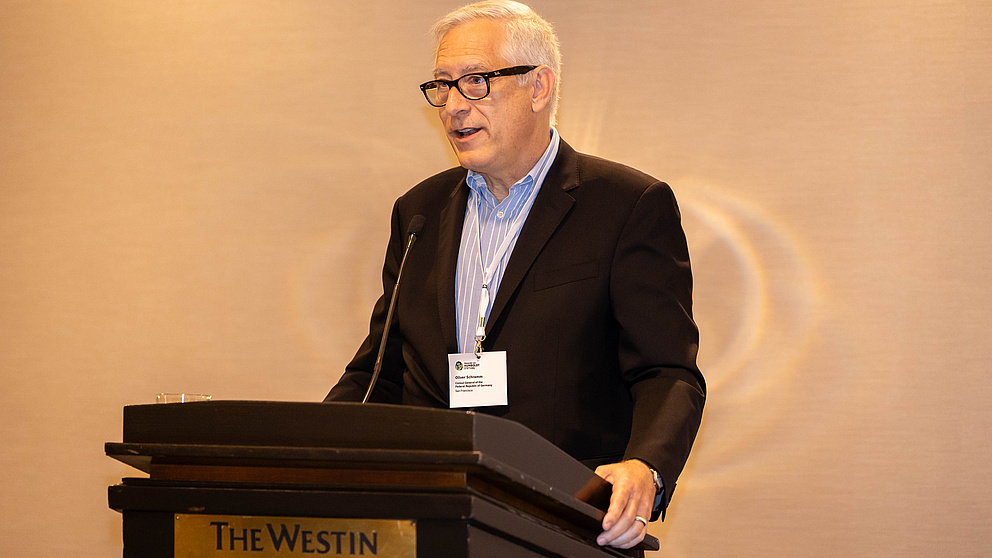 Ein Mann steht auf einer Bühne hinter einem Rednerpult und spricht zum Publikum.