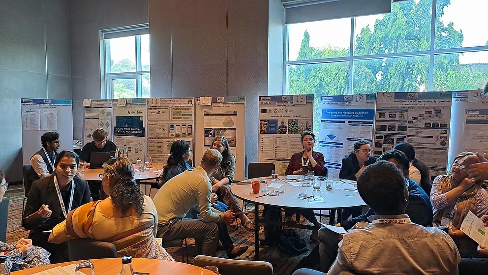 Teilnehmer eines Symposiums sitzen an einem Tisch, während sie sich über verschiedene Forschungsprojekte austauschen und Notizen machen.