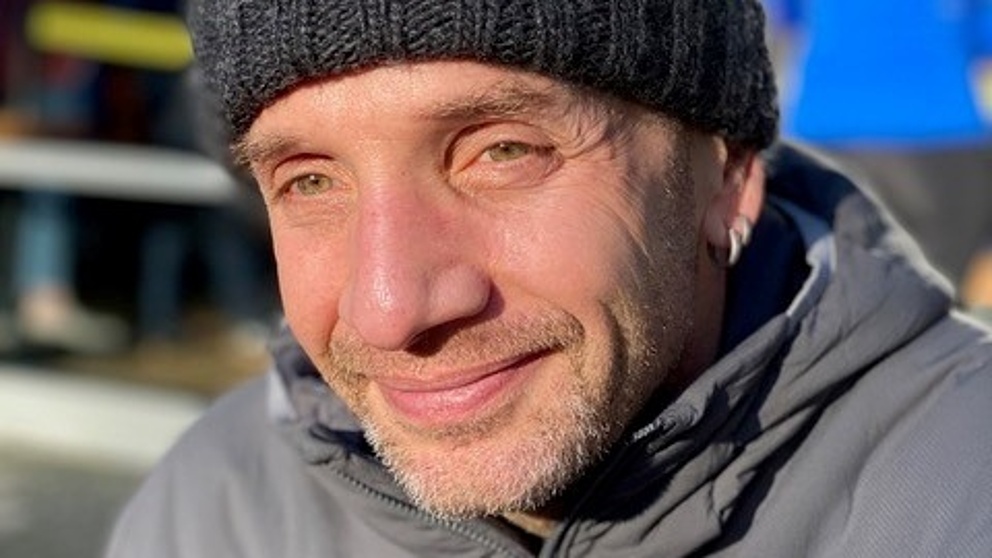 Portrait eines lächelnden Mannes mit grauer Mütze und grauer Jacke. 