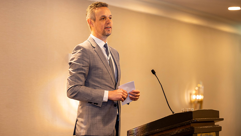 Ein Mann auf einer Bühne hinter einem Rednerpult spricht zum Publikum.